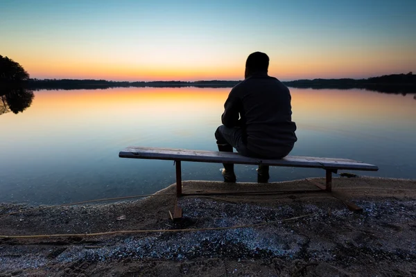 Mann sitzt bei Sonnenuntergang auf Bank am Seeufer — Stockfoto