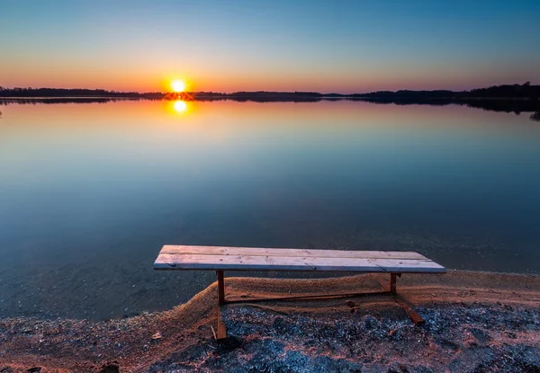 Göl kıyısı batımında bankta — Stok fotoğraf