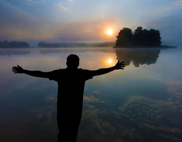 Mann beobachtet einen Sonnenaufgang über dem See. Menschensilhouette. — Stockfoto