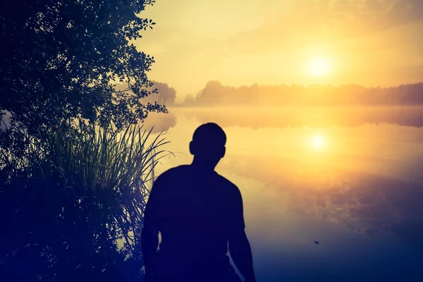 Mann beobachtet einen Sonnenaufgang über dem See. Menschensilhouette. — Stockfoto