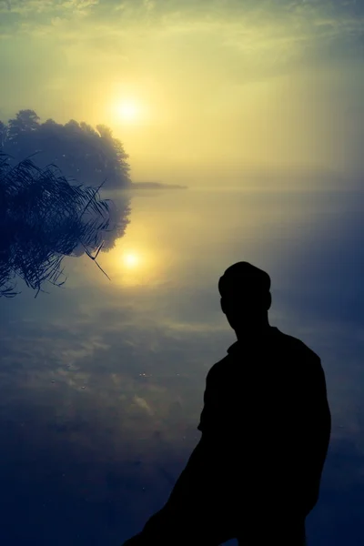 Człowiek ogląda wschód słońca nad jeziorem. Sylwetka człowieka. — Zdjęcie stockowe