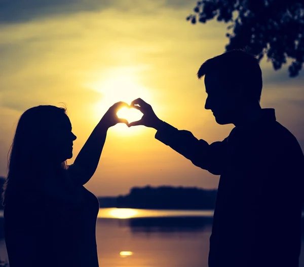 Pareja haciendo forma de corazón con sus manos en la orilla del lago. — Foto de Stock