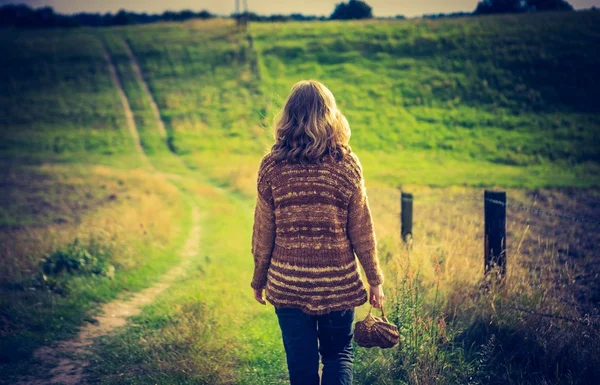 Meisje in de trui lopen door landelijke met gras begroeide weg — Stockfoto