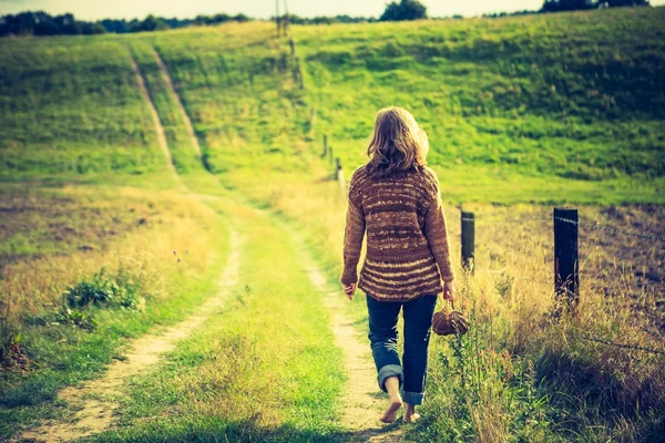 Meisje in de trui lopen door landelijke met gras begroeide weg — Stockfoto