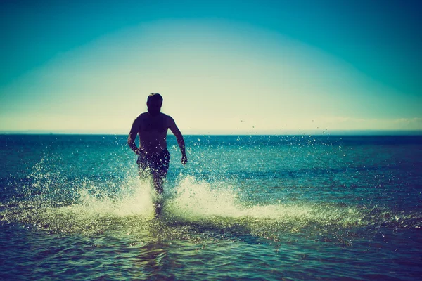 Silhouette eines Mannes, der im Meerwasser durch den Strand läuft — Stockfoto