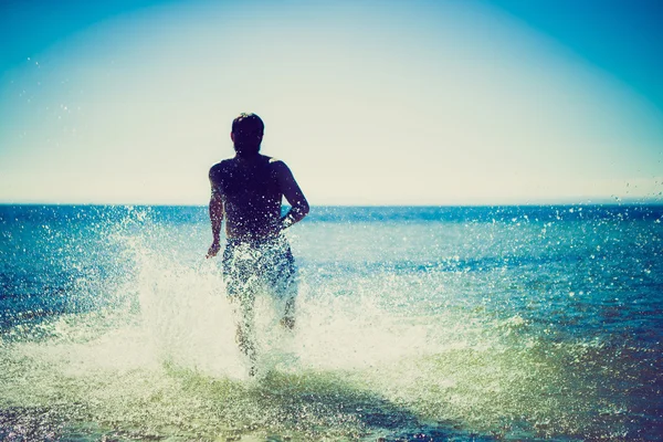 Silhouette eines Mannes, der im Meerwasser durch den Strand läuft — Stockfoto