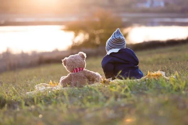 Petit garçon et son ours en peluche assis sur une couverture près du lac — Photo