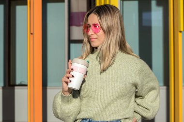 Kahve fincanı ve pembe güneş gözlüklü genç kadın.