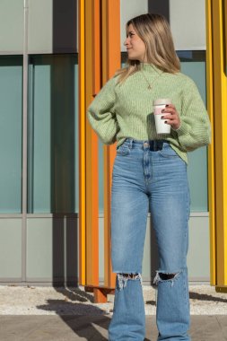 Kahve fincanı ve renkli şehir geçmişi olan genç bir kadın.