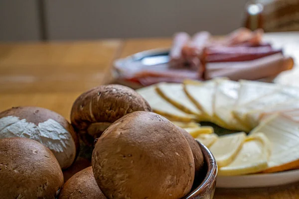 Fransız raketinin tüm tipik malzemeleri, Fransız peynirlerinin çeşitleri, haşlanmış patatesler, havuçlar, mantarlar, salatalıklar ve sosisler, doğal ışık altında ve kırsal bir sunum.