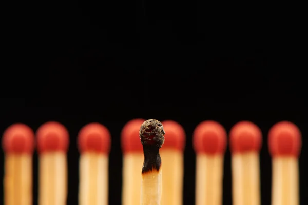 Burnt match in front of eight red wooden matches — Stock Photo, Image