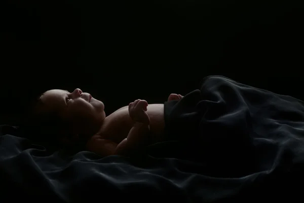 Cute baby lying covered with black fabric, isolated on black