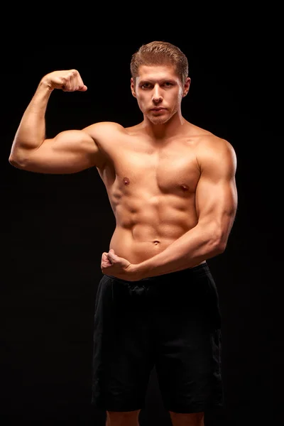 Powerful sportsman demonstrating biceps, isolated on black background — 图库照片