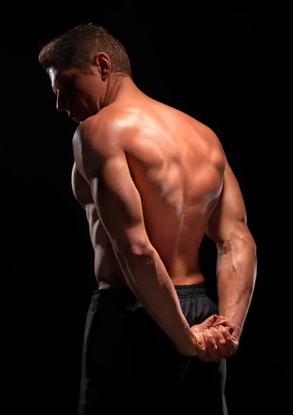 Rear view of shirtless sportsman demonstrating back, pectoral, abs muscles