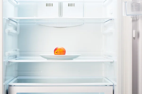 Peach on white plate in open empty refrigerator — Stock Photo, Image