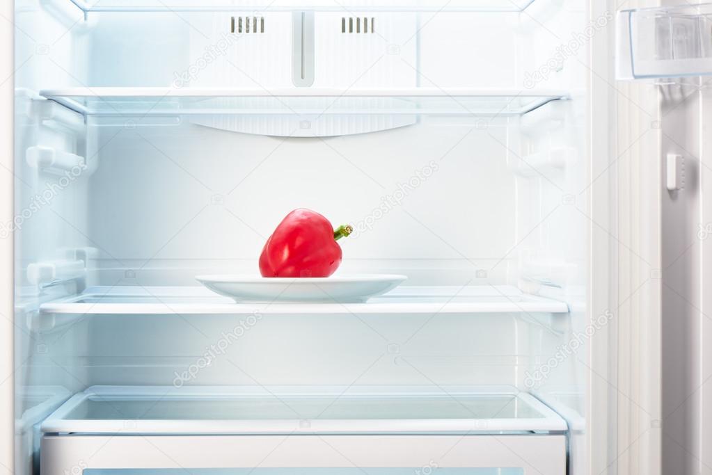 Red pepper on white plate in open empty refrigerator