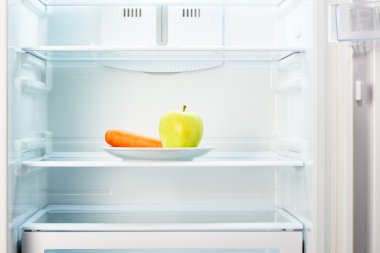 Yeşil elma ve portakal havuç buzdolabında beyaz plaka üzerinde