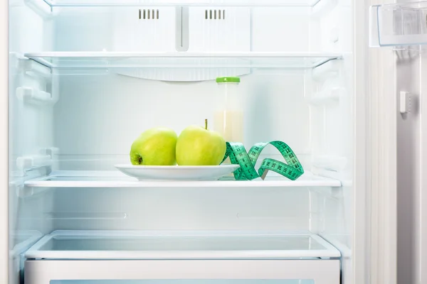 Two apples with measuring tape and glass bottle in refrigerator — Stock Photo, Image