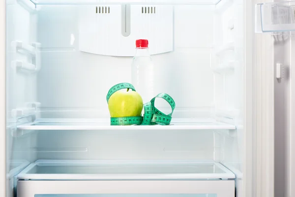 Яблоко с измерительной лентой и бутылкой на полке холодильника — стоковое фото