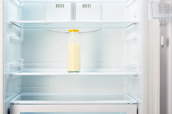 Glass bottle of yoghurt on shelf of open empty refrigerator — Stock Photo, Image