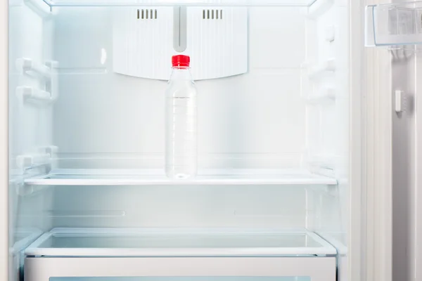 Бутылка воды на полке открытого пустого холодильника — стоковое фото