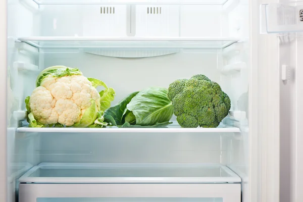 Cauliflower, green cabbage and green broccoli on shelf of open empty refrigerator