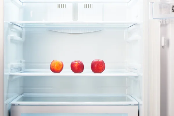 Три двухцветных оранжевых и красных персика на полке открытого пустого холодильника — стоковое фото