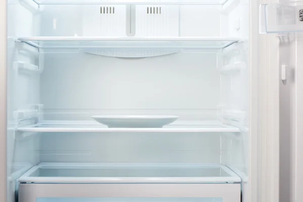 Empty white plate in open empty refrigerator — Stock Photo, Image