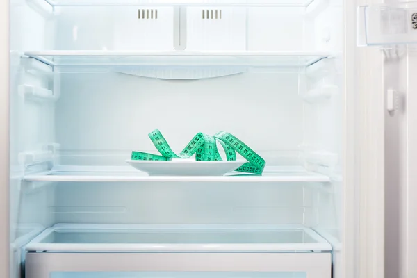 Fita métrica verde na placa branca no refrigerador vazio aberto — Fotografia de Stock