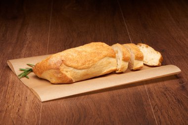 Koyu ahşap masa üzerinde fırın kağıt üzerinde ciabatta ekmeği ve biberiye dilimlenmiş