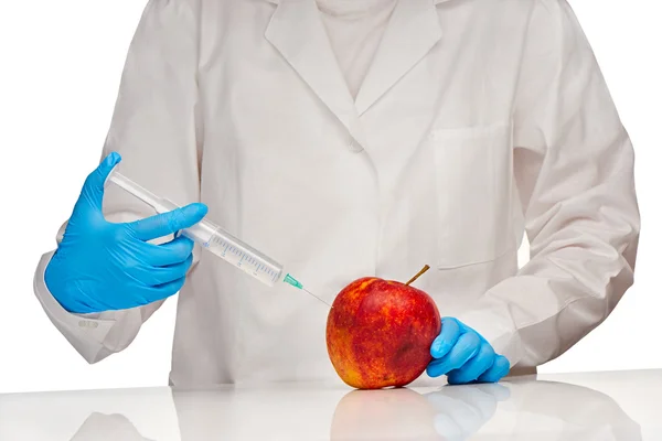 Female doctor in white medical gown and blue sterilized surgical gloves makes injection to bad looking apple with plastic syringe — Stock Photo, Image