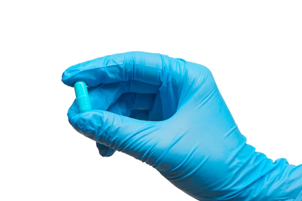 Vrouwelijke arts hand in blauwe gesteriliseerde chirurgische handschoen bedrijf blauwe capsule tegen witte achtergrond — Stockfoto