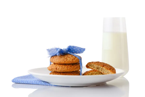 Oatmeal cookies tied with blue ribbon in small white polka dots and halves of cookies on white ceramic plate on blue napkin and glass of milk — Stock Photo, Image