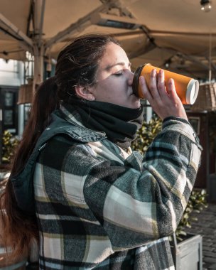Güneşli bir kış gününde kahve içen bir kadın.