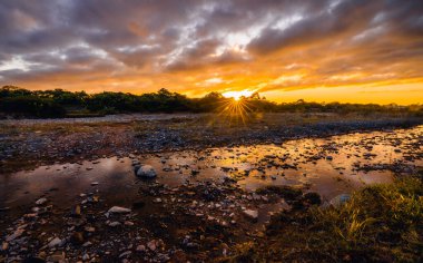 Güneşin yıldız şeklinde olduğu taşlı bir nehirde inanılmaz bir gün doğumu.