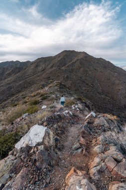 Genç bir kadın bir dağda dar bir yolda yürüyor.