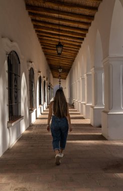 Sırtı bir galeride yürüyen Latin kökenli genç bir gezgin kız.