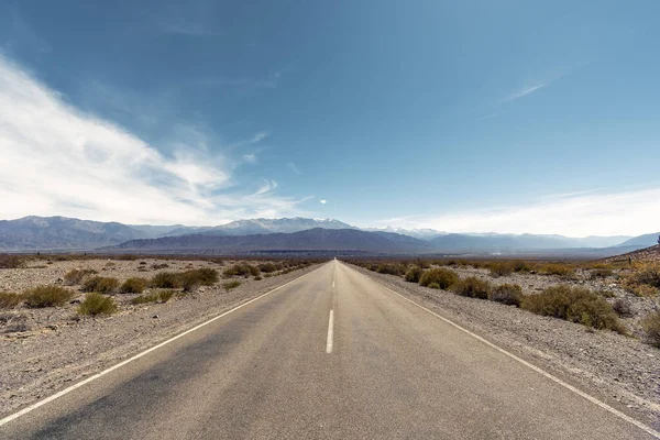 Two lane road in a arid landscape in Argentina leading to mountains against blue sky — Stock Photo, Image
