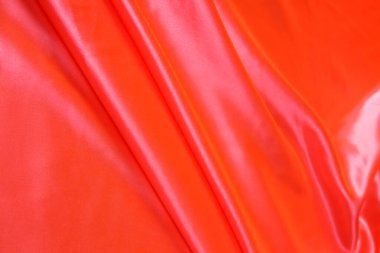 Renkli turuncu tekstil kumaşı kıvrımlar ve dalgalar halinde kıvrılmış, parlak ışık ve desen parıldıyor.