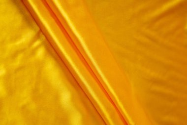 Renkli sarı tekstil kumaşı kıvrımlar ve dalgalar halinde kıvrılmış, parlak ışık ve desen parıldıyor.