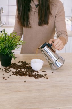 Hafif bir İskandinav mutfağındaki kadın sabahları kahve makinesinden fincana kahve döker.