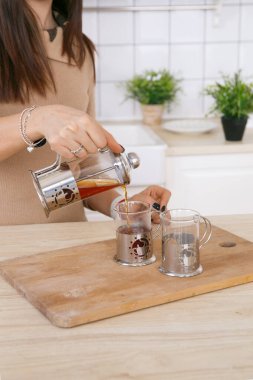 Hafif İskandinav mutfağındaki bir kadın sabahları çaydanlıktan fincana çay doldurur.