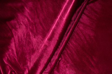 Renkli kırmızı tekstil kumaşı kıvrımlar ve dalgalar halinde kıvrılmış, parlak ışık ve desen parıldıyor.