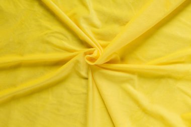 Renkli sarı tekstil kumaşı kıvrımlar ve dalgalar halinde kıvrılmış, parlak ışık ve desen parıldıyor.