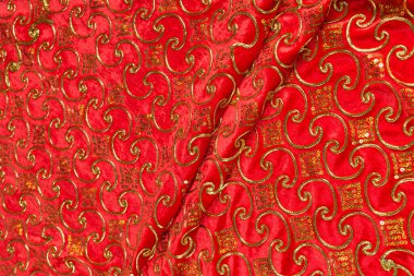 Renkli kırmızı tekstil kumaşı kıvrımlar ve dalgalar halinde kıvrılmış, parlak ışık ve desen parıldıyor.