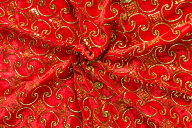 Renkli kırmızı tekstil kumaşı kıvrımlar ve dalgalar halinde kıvrılmış, parlak ışık ve desen parıldıyor.