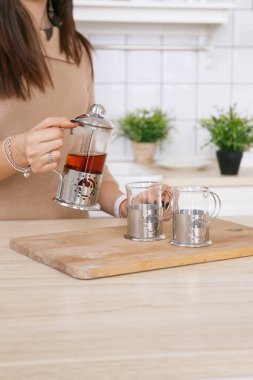 Hafif İskandinav mutfağındaki bir kadın sabahları çaydanlıktan fincana çay doldurur.