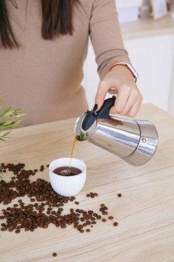 Hafif bir İskandinav mutfağındaki kadın sabahları kahve makinesinden fincana kahve döker.