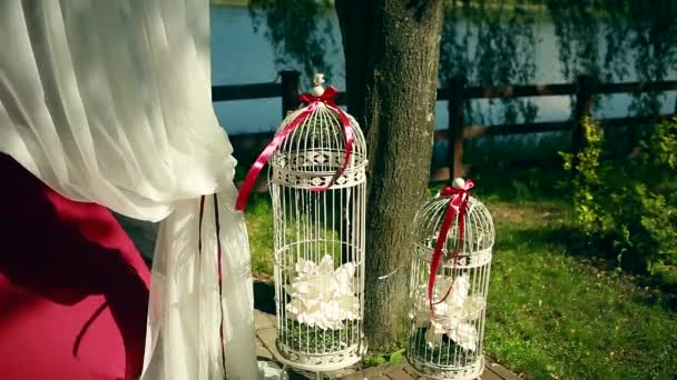 Hermosa decorada con lámpara de araña de gasa blanca clara y ramos de rosas colores pastel sillas del pabellón de boda y mesa de pie sobre hierba verde cerca del lago y los árboles día soleado, imagen horizontal — Vídeo de stock