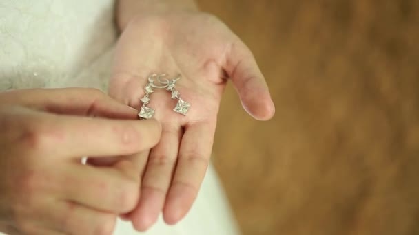 Pendientes de boda en una mano femenina, ella toma los pendientes, la novia honorarios mañana novia, vestido blanco, llevar pendientes — Vídeo de stock